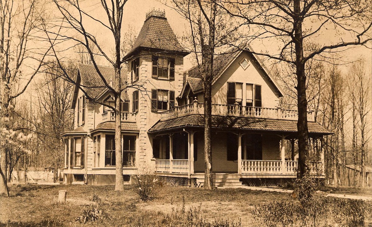 Historic house with a tower and decorative porch, shown in a sepia photograph.